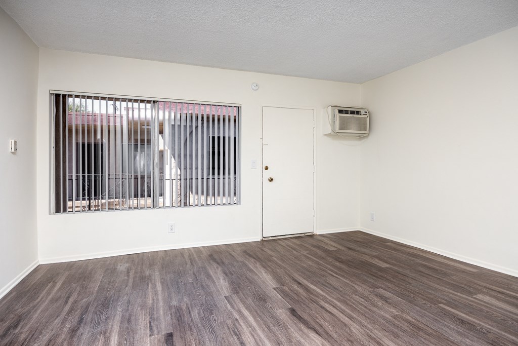 the living room of an apartment with a large window and wood flooring