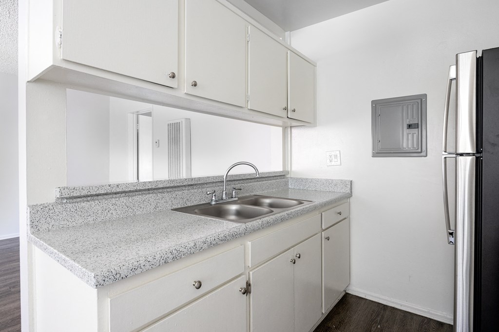an empty kitchen with white cabinets and a sink and refrigerator