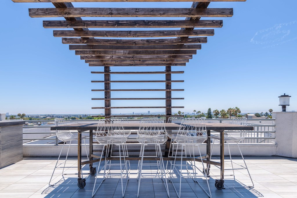 a view of the roof deck with a wooden pergola and white chairs