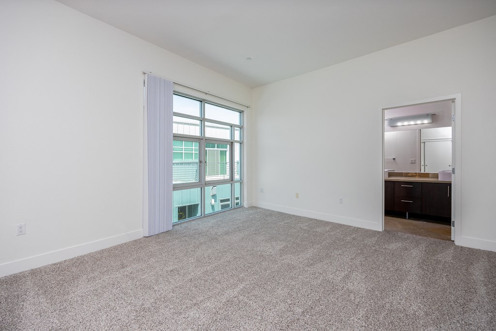 an empty living room with white walls and carpeting and a window