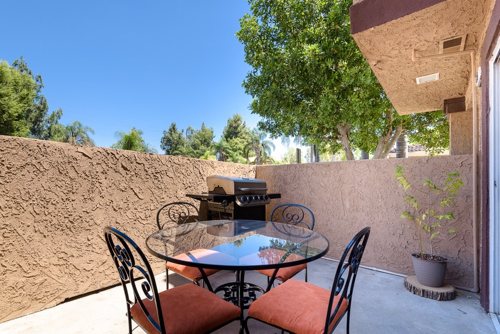 a patio with a glass table and chairs and a grill