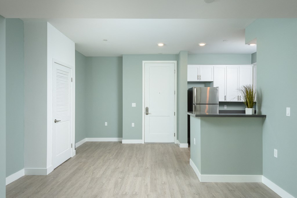 an empty living room with a kitchen and a door