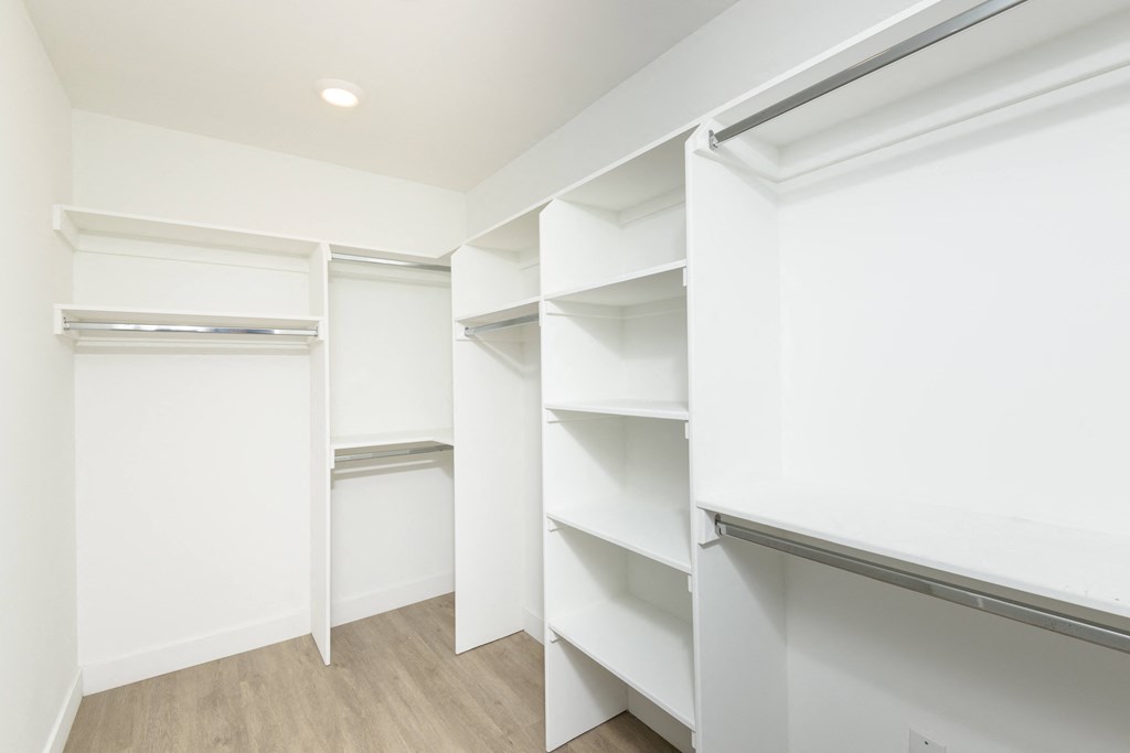 a walk in closet with white walls and shelves and a wood floor