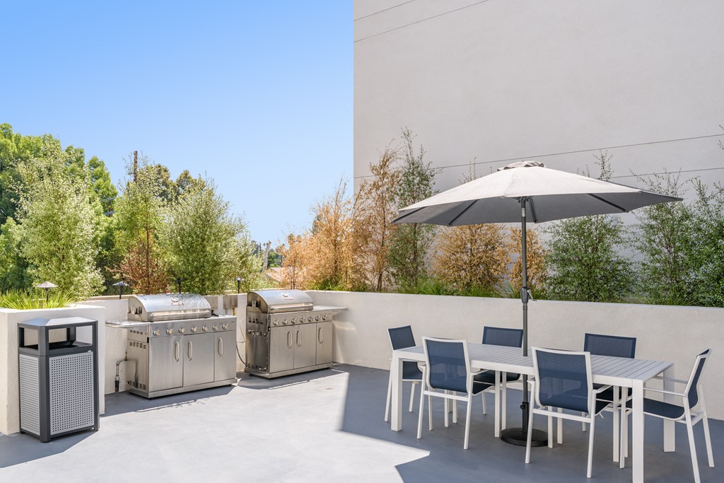 a patio with tables and chairs and barbecue grills and an umbrella