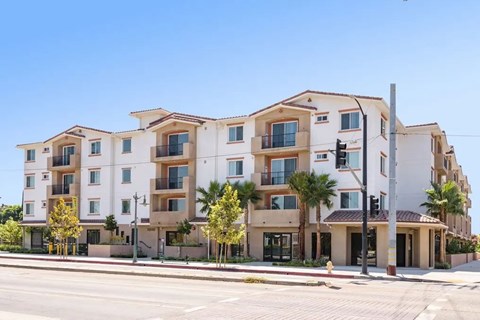 A row of modern apartment buildings with balconies and trees in front.