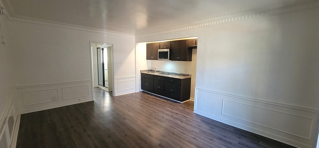 an empty living room with wood floors and a kitchen