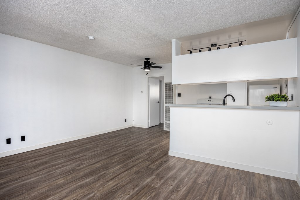 an empty living room and kitchen with white walls and wood flooring