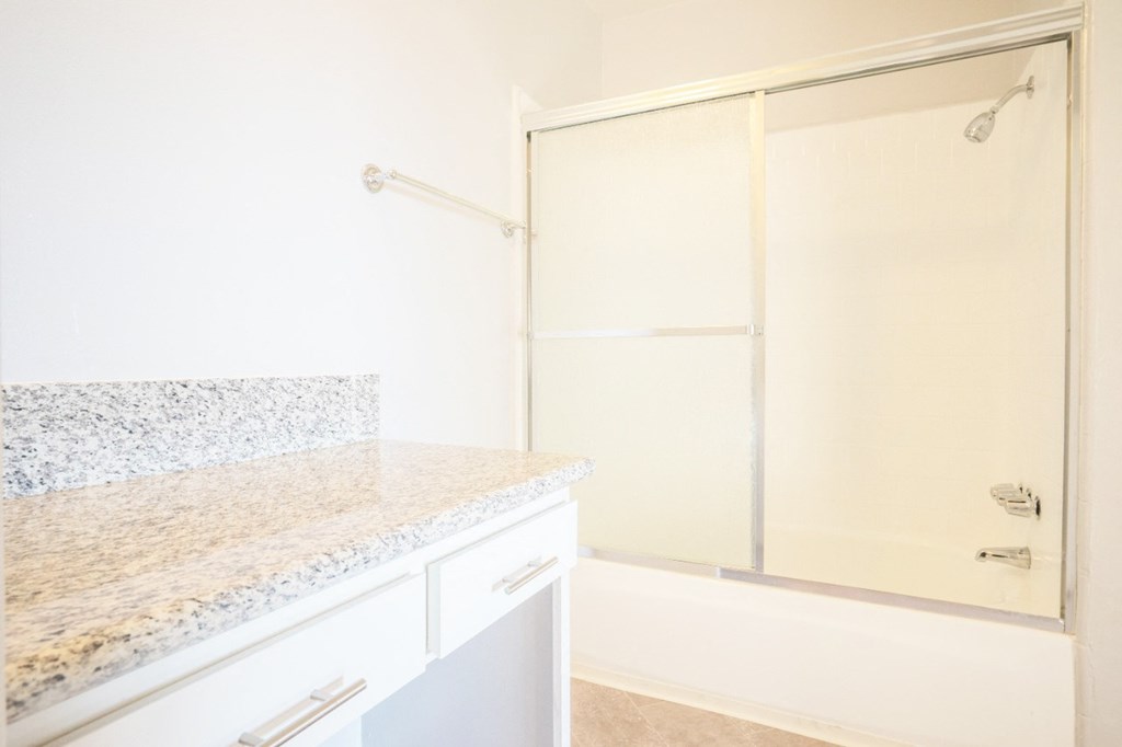 a white bathroom with a shower and a granite counter top
