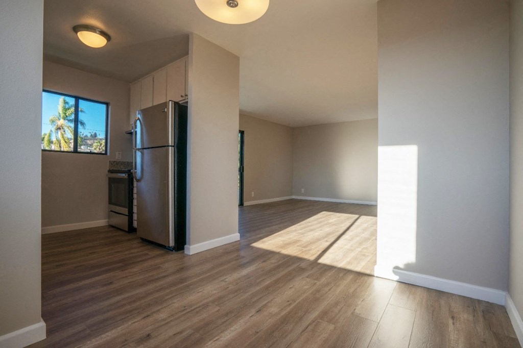 an empty living room with a refrigerator and a window