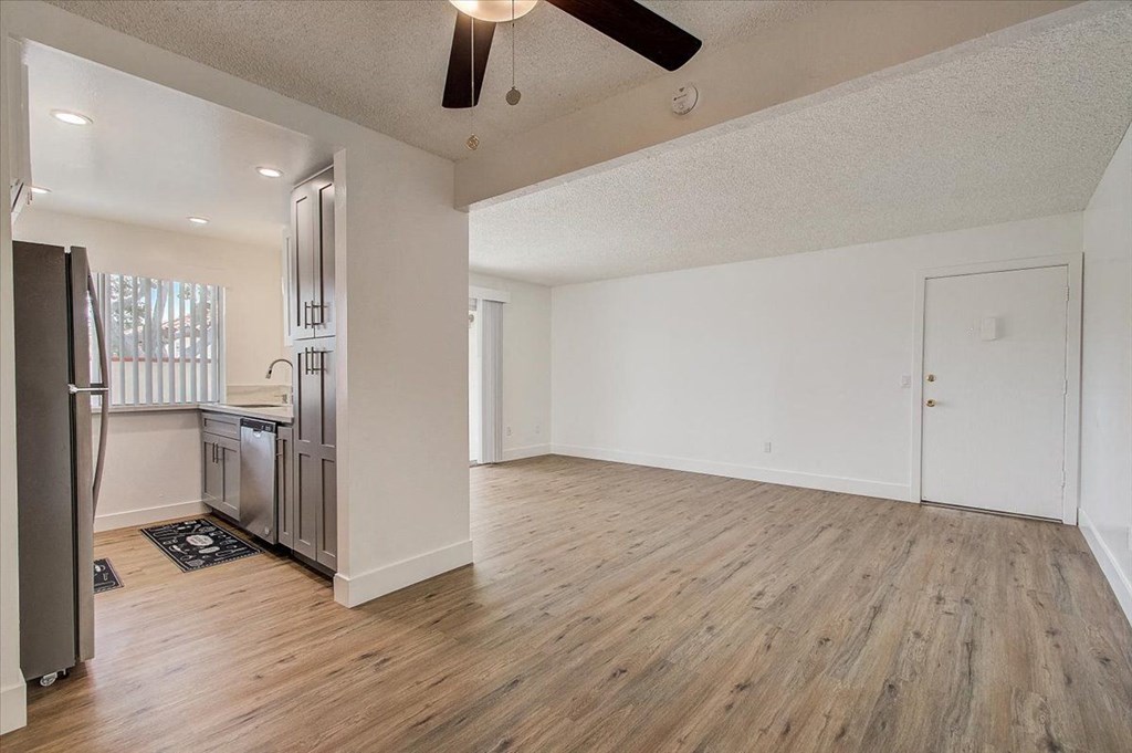 an empty living room with a kitchen in the background