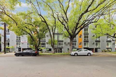 A black car is parked on the left side of a street, and a silver car is parked on the right side.