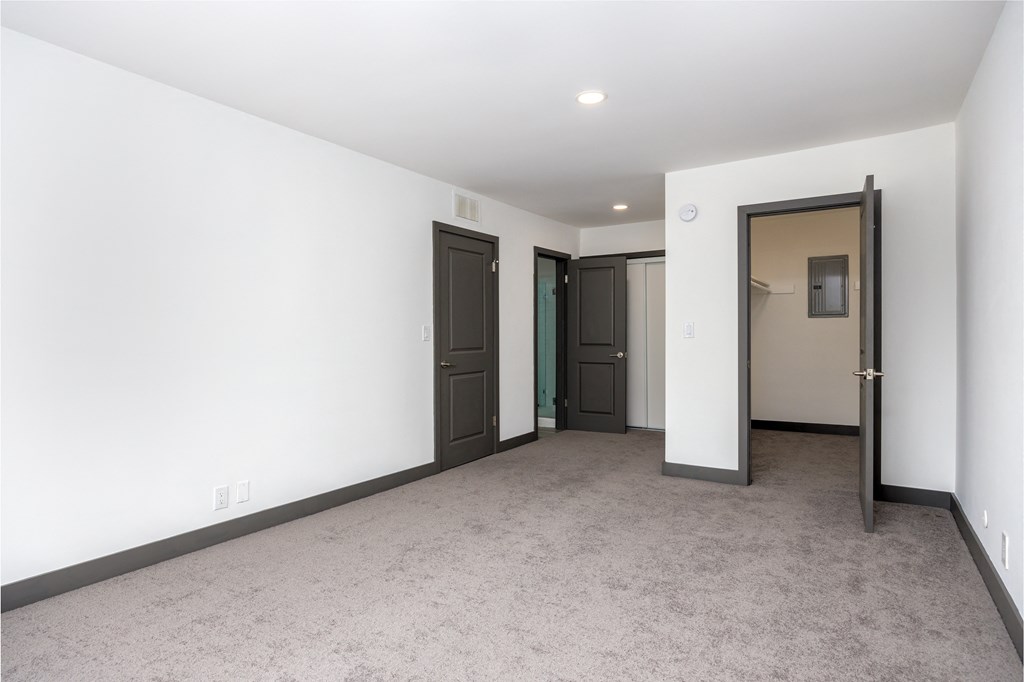 an empty living room with white walls and grey carpet and two doors to different rooms