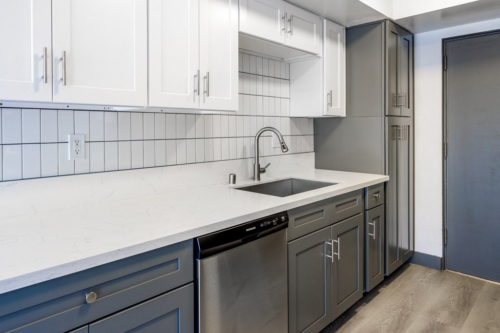 an empty kitchen with white countertops and a stainless steel sink
