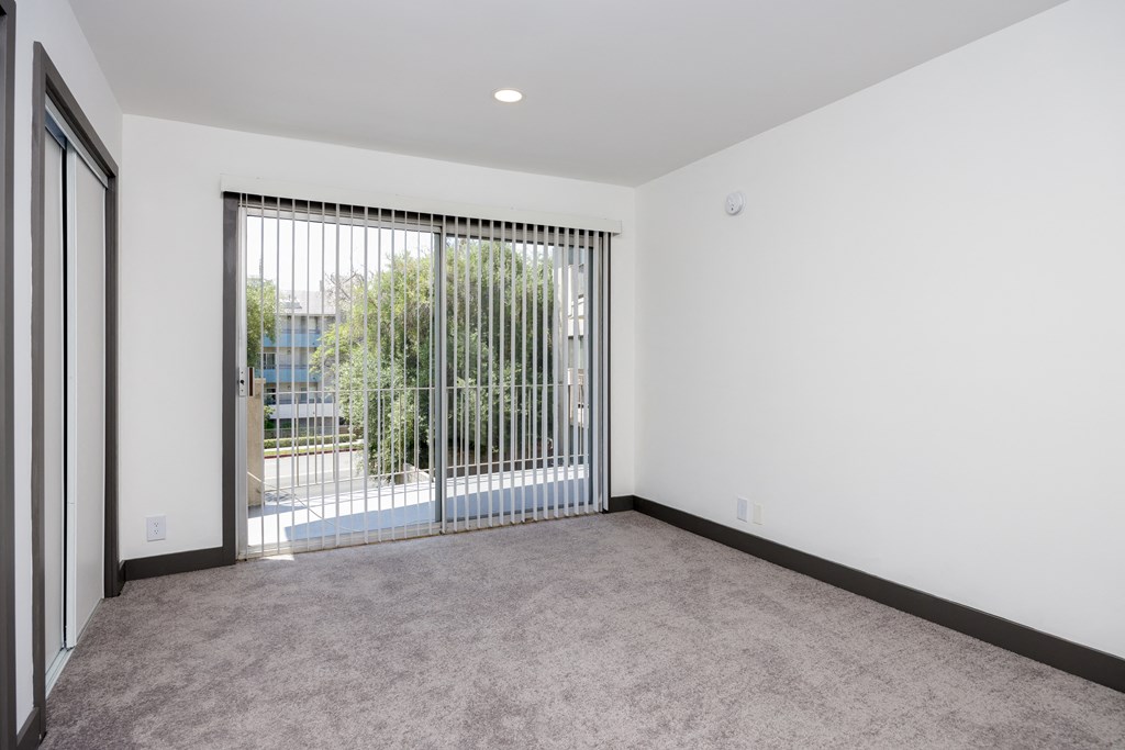 an empty living room with a sliding glass door to a balcony