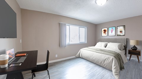 A bedroom with a bed, a desk with a laptop and a cup on it, a chair, and pictures on the wall.