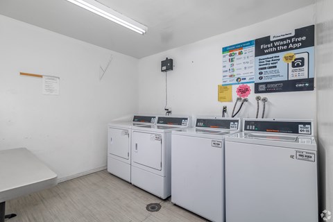 A laundromat with a sign that says "First Wash Free with the App" and several washing machines.