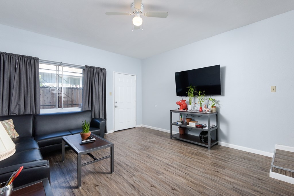 A living room with a black couch, a glass coffee table, and a flat screen TV mounted on the wall.