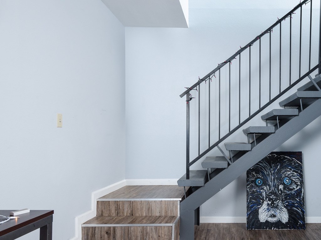 A painting of a dog with blue eyes is on the wall next to a staircase.