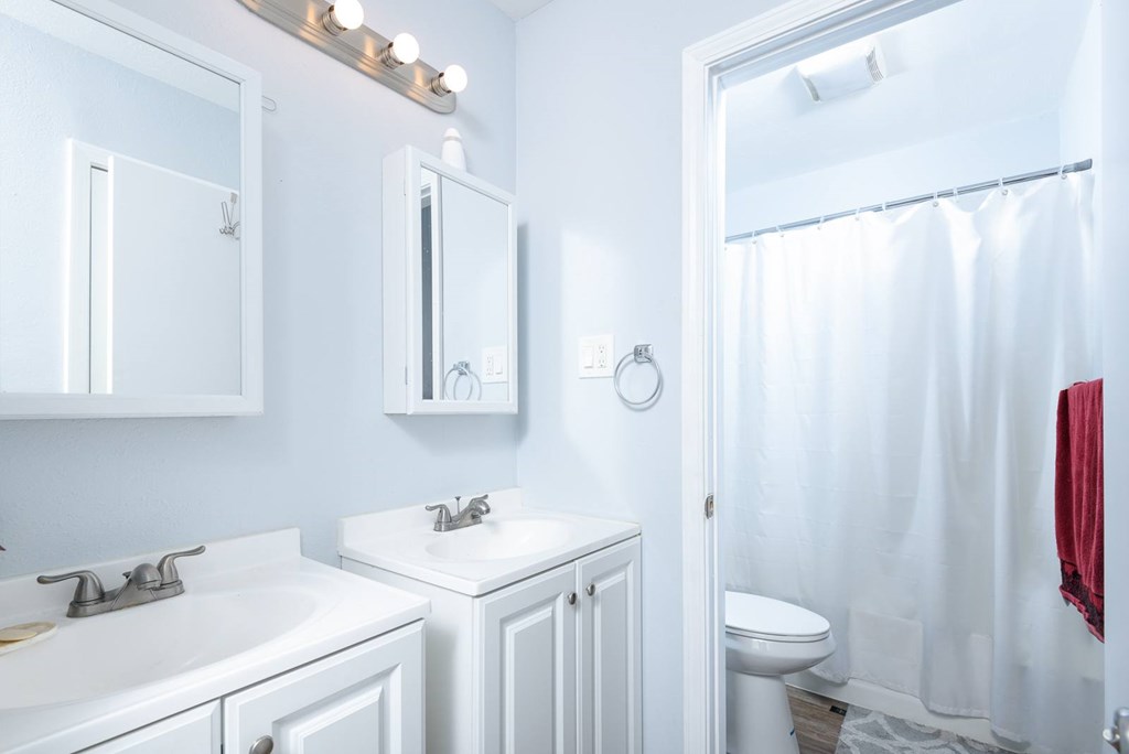 A white bathroom with a sink, mirror, toilet, and shower.