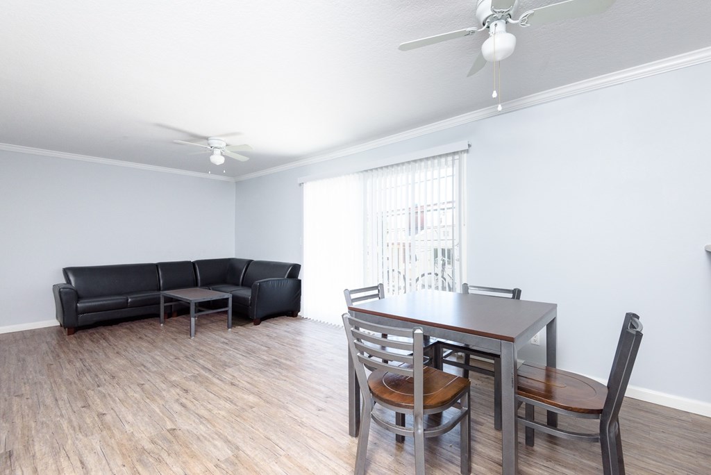 A living room with a black couch, a wooden dining table, and a ceiling fan.