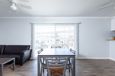 A black leather couch sits in a living room with a wooden dining table and chairs.
