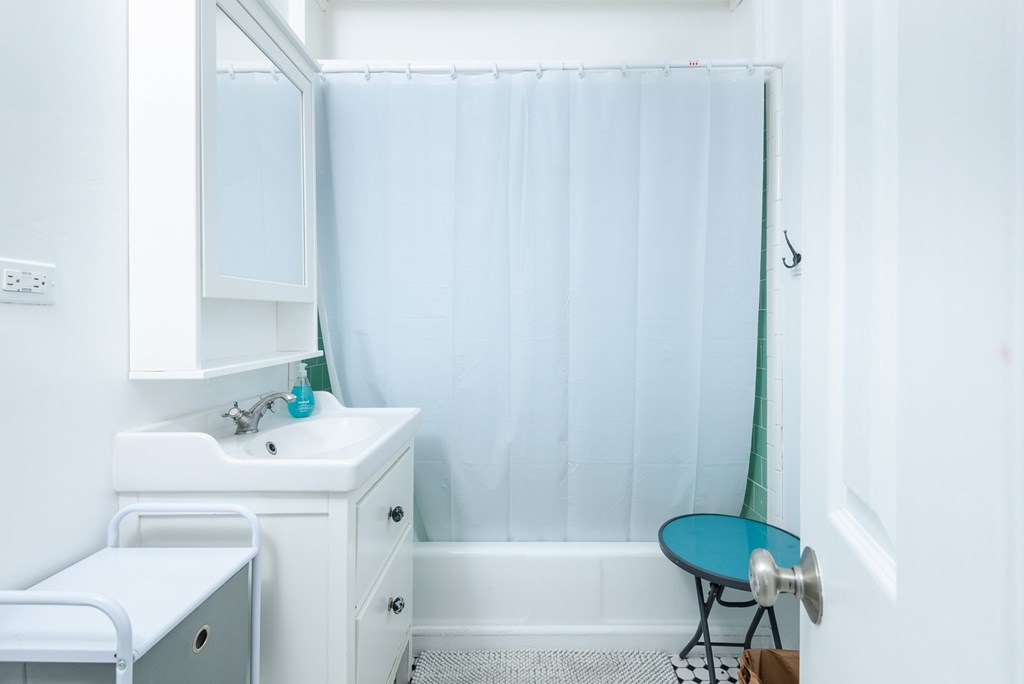 A small bathroom with a white sink and a blue chair.