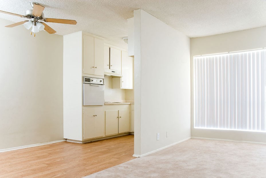 an empty living room with a kitchen with a ceiling fan
