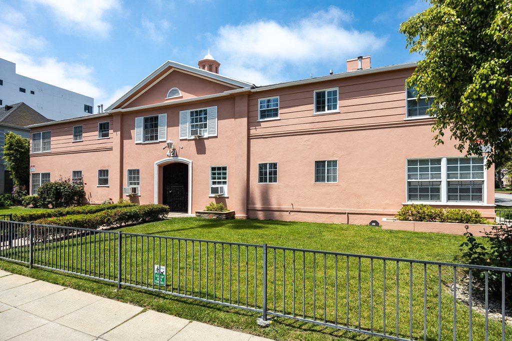 a pink building with a green lawn and a metal fence in front of it