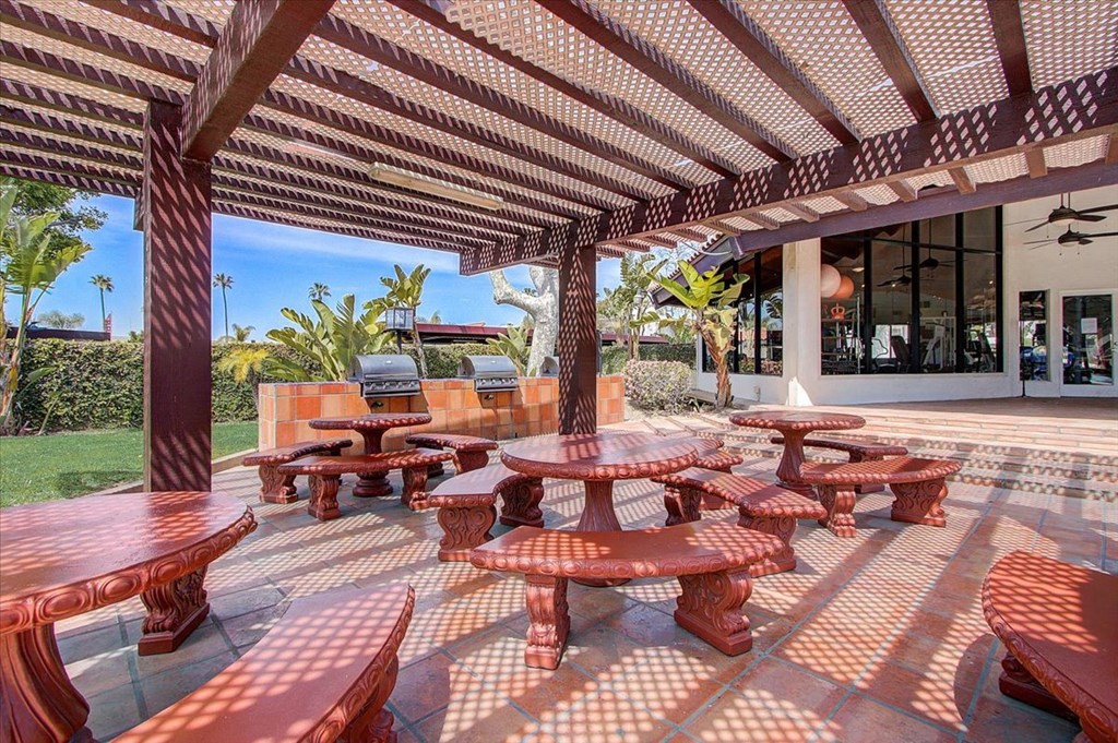 a patio with tables and benches and a pool in the background