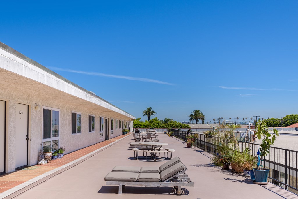 the terrace of a building with tables and chairs and the ocean in the background