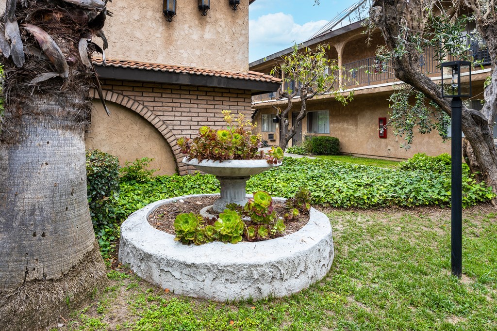 a fountain sits in the middle of a grassy area in front of a building
