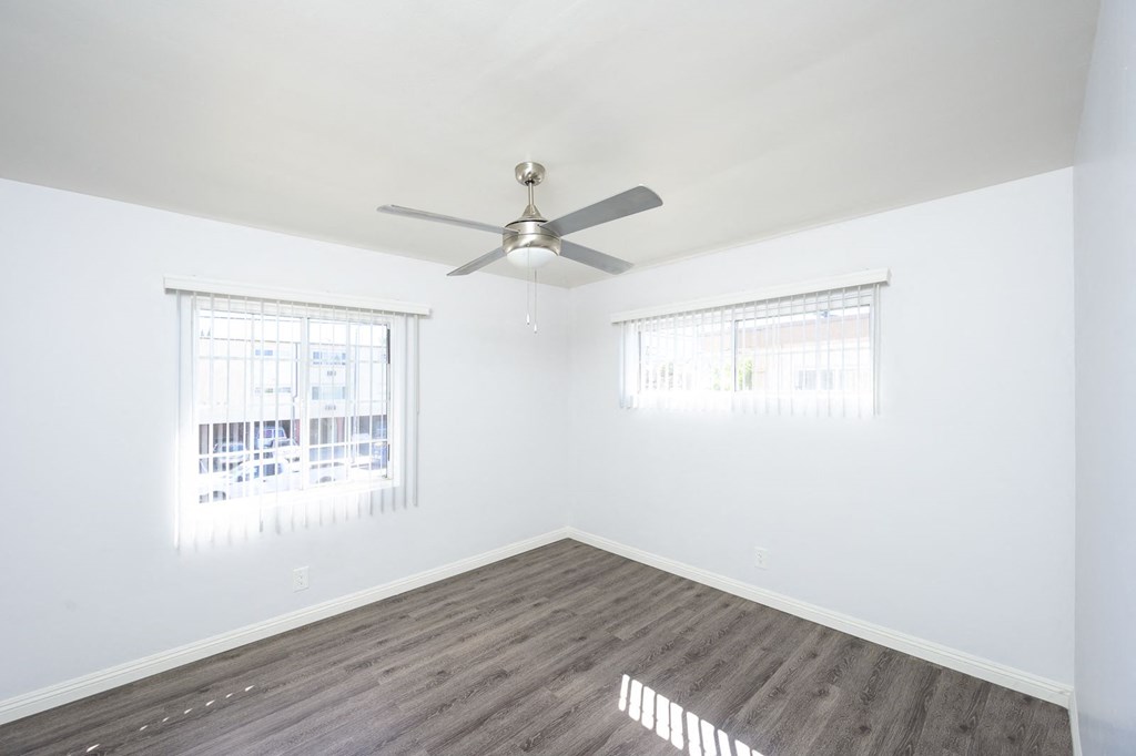 an empty bedroom with a ceiling fan and two windows