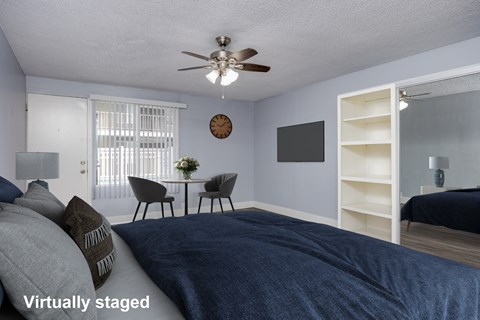 A bedroom with a bed, a table with chairs, a clock, and a shelf.