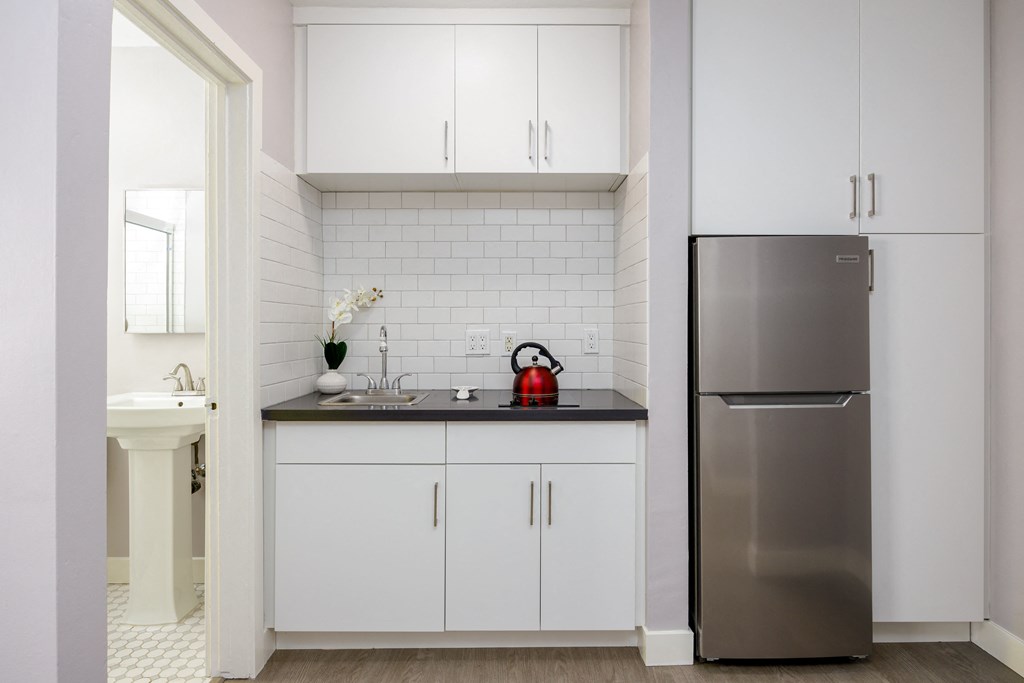 a small kitchen with white cabinets and a stainless steel refrigerator