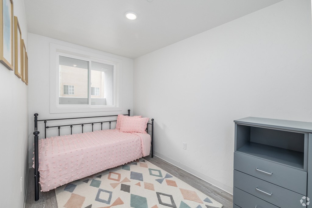 A bedroom with a pink bedspread and a grey filing cabinet.