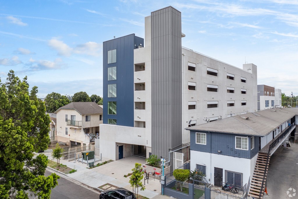 A modern building with a grey and blue exterior stands tall in the foreground of a residential area.
