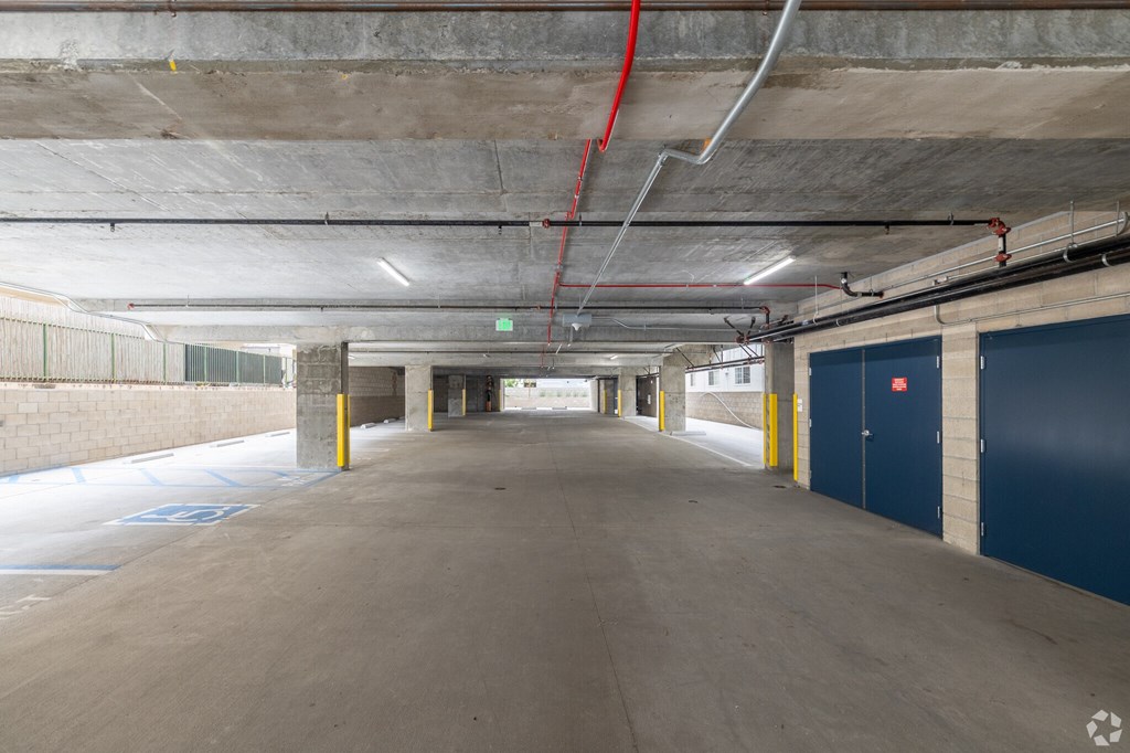 A long, empty parking garage with a red hose running along the ceiling.