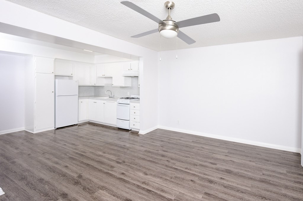 an empty living room with a ceiling fan and a kitchen