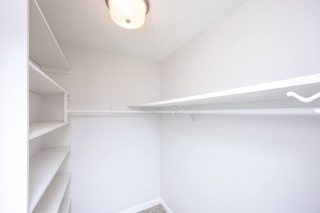 a walk in closet with white walls and shelves and a light