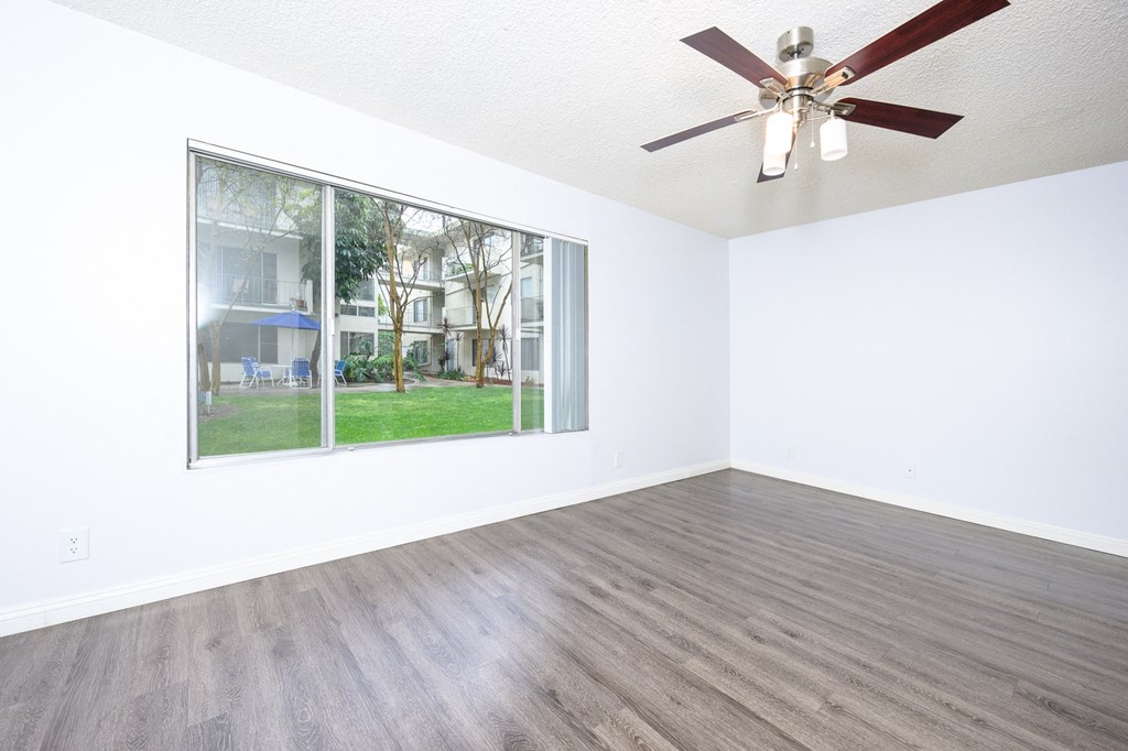 an empty living room with a large window and a ceiling fan