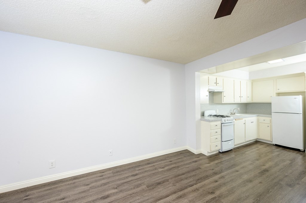 an empty living room and kitchen with white walls and wood flooring