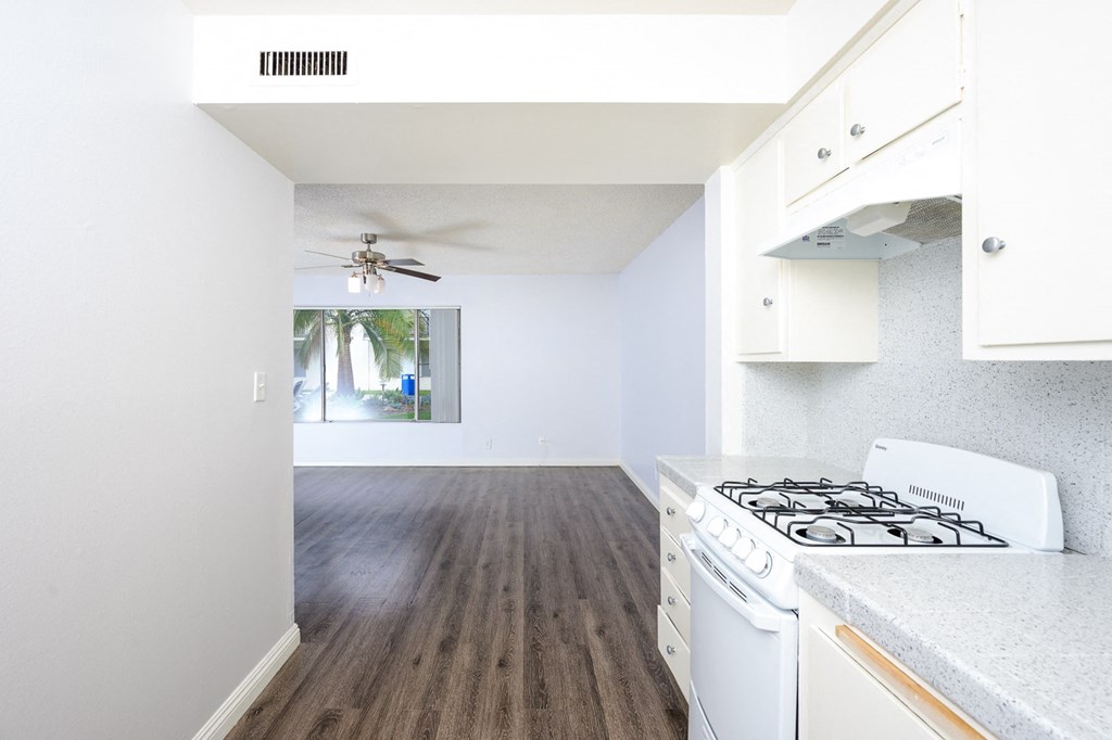 an empty kitchen and living room with white appliances and a ceiling fan