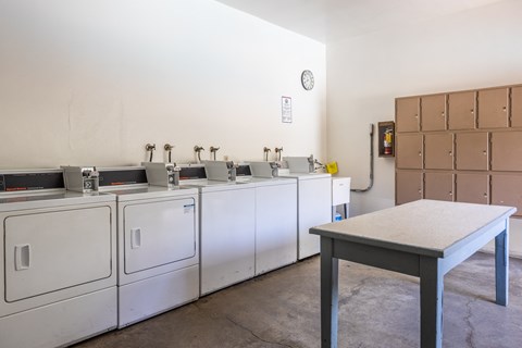 a row of washers and dryers in a room with a table in the foreground
