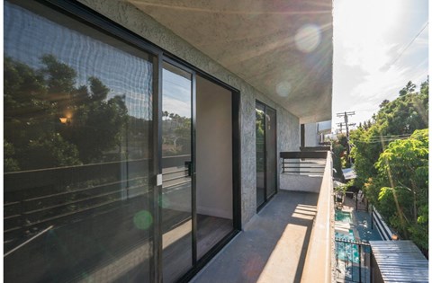 a balcony with glass doors and a view of trees and a pool