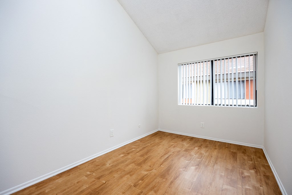 the spacious living room of an apartment with wood flooring and a window