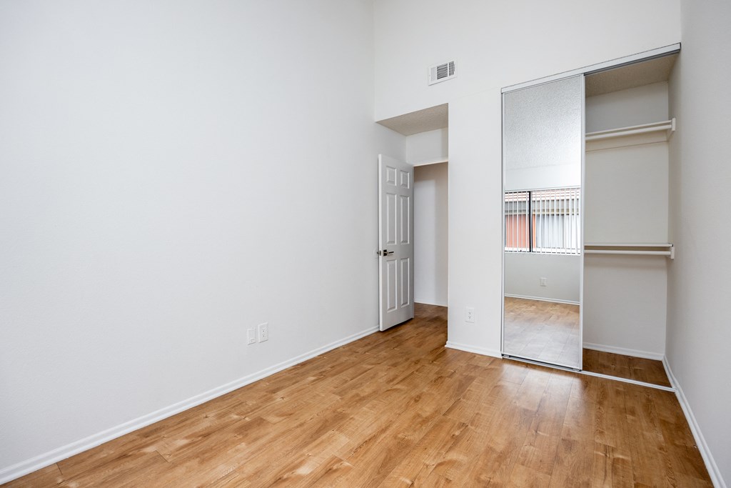 an empty room with wood flooring and a mirrored closet