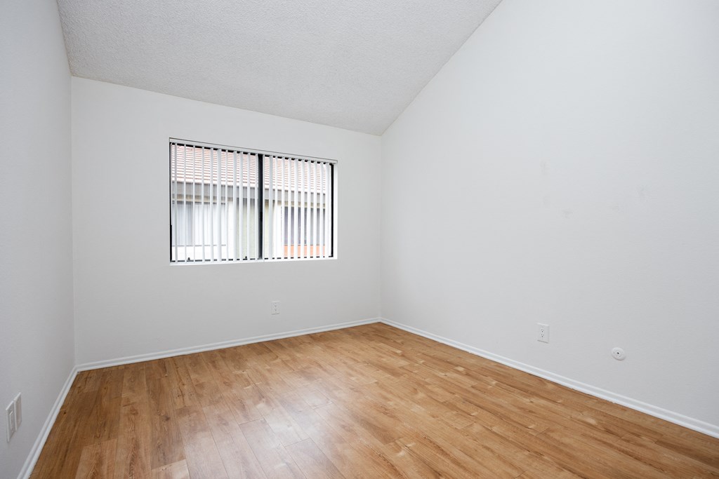 the spacious living room of an apartment with wood flooring and a window