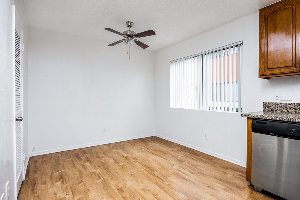 an empty living room with a ceiling fan and a kitchen