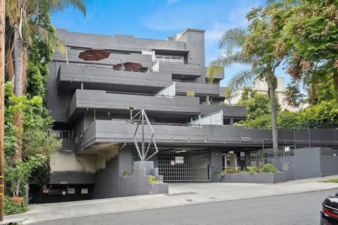 A modern building with a grey facade and palm trees in front.