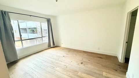 A room with wooden flooring and a large window with grey curtains.